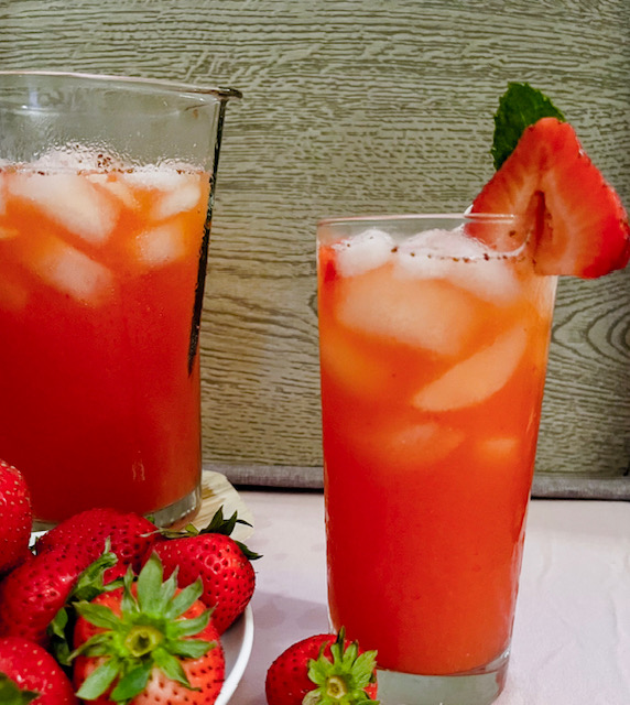 Sparkling strawberry lemonade served with ice, a strawberry slice, and a mint leaf.