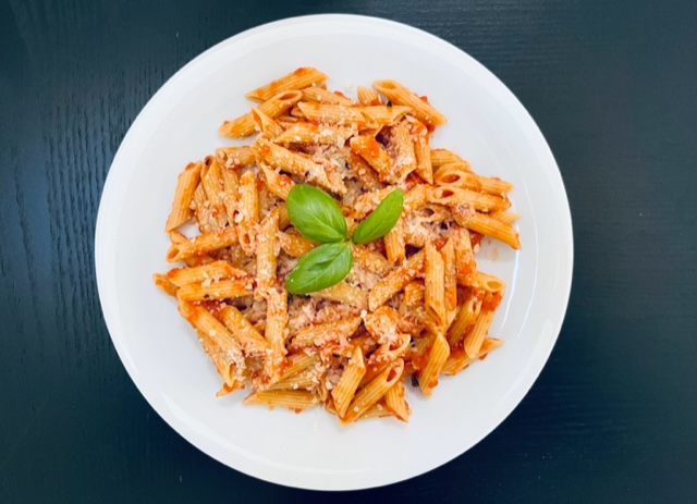 Penne pasta with tomato sauce topped with parmesan cheese and basil leaves